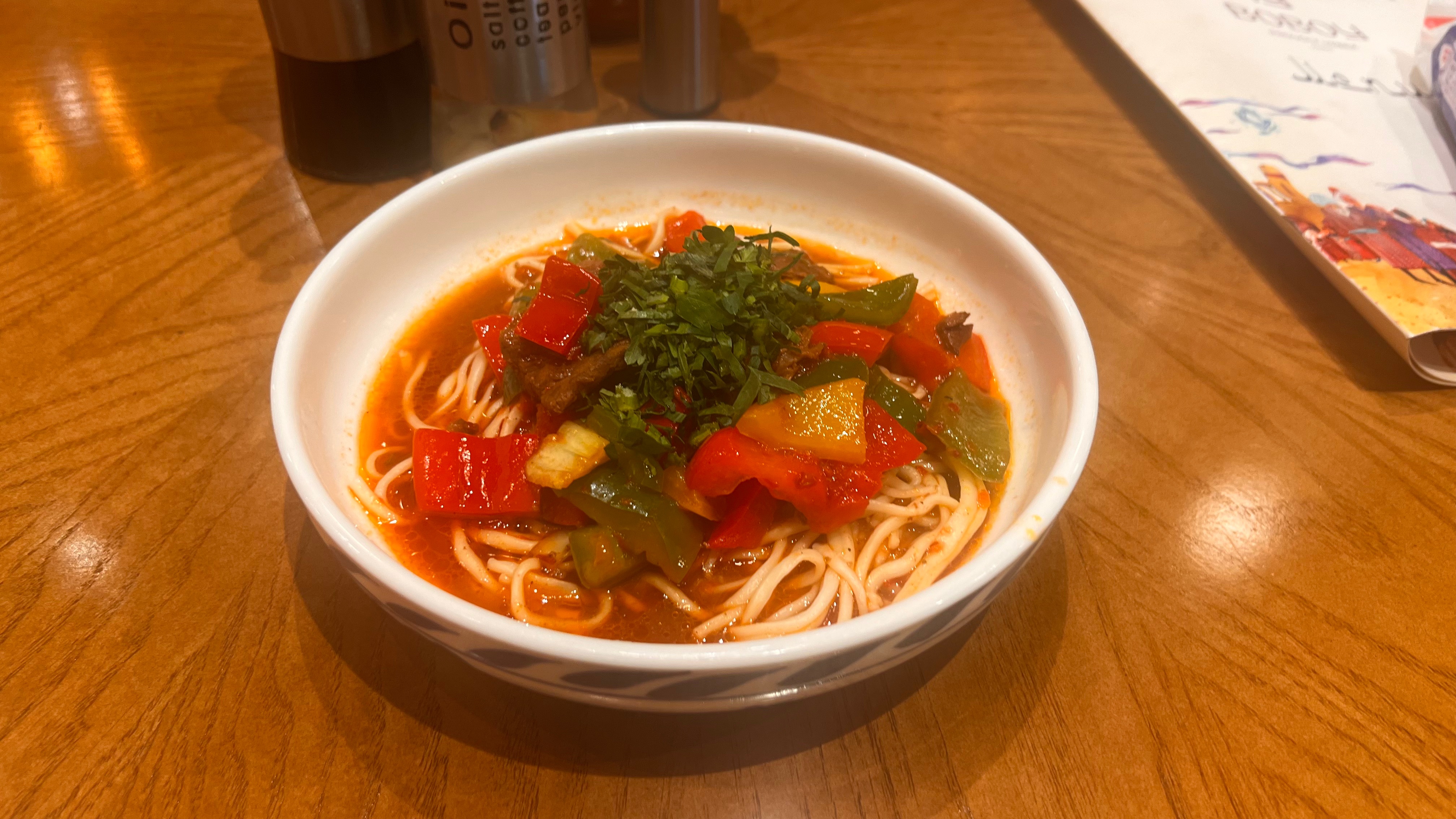 赤いパプリカと緑のピーマンがトッピングされた、スープに入った細い麺のボウル